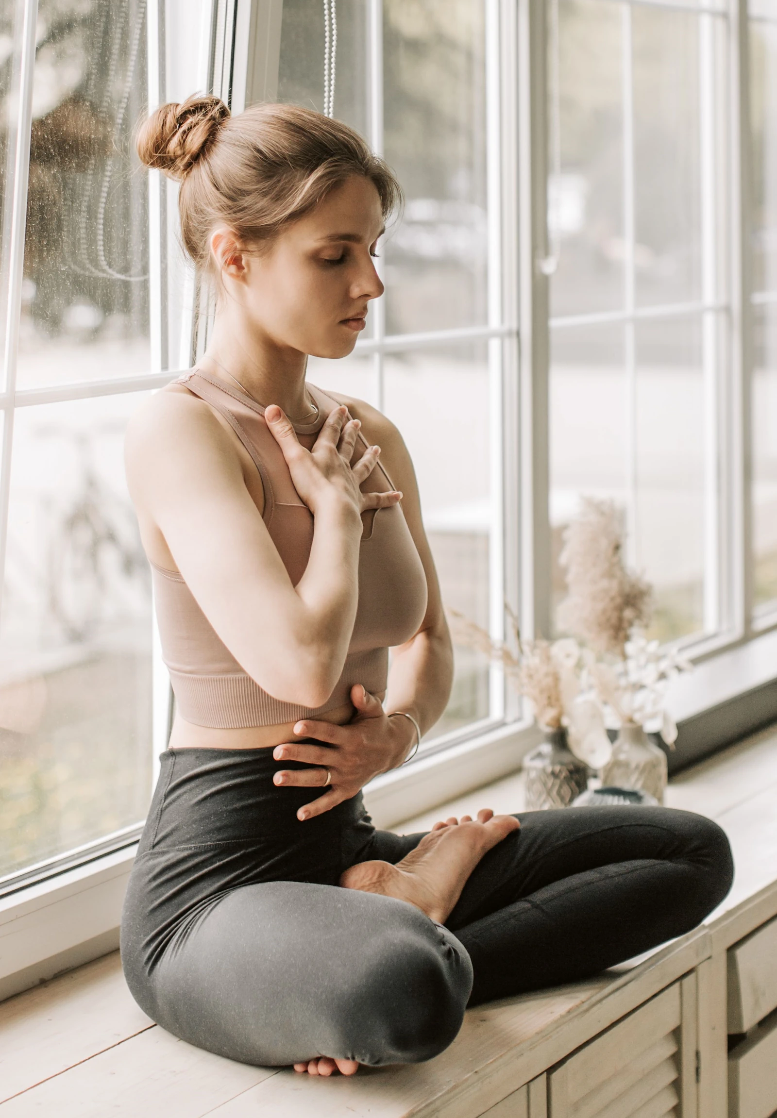 Mujer meditando y respirando junto a una ventana con luz solar